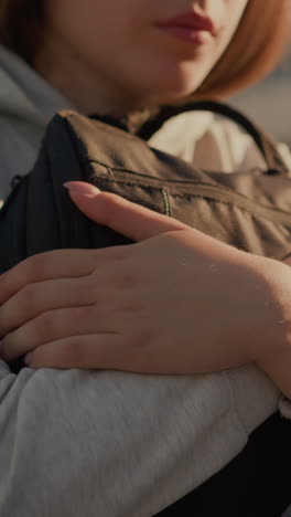 primer plano de una mujer joven sosteniendo su bolsa estrechamente con la luz del sol proyectando reflejos cálidos en sus manos y vaqueros, creando una sensación de soledad e introspección