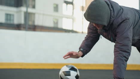 hombre realizando flexiones alternando la colocación de la mano en la pelota de fútbol mostrando fuerza, coordinación y agilidad en una arena urbana al aire libre con fondo de edificio residencial