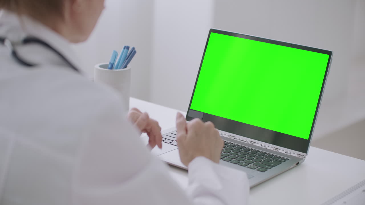 la mujer médico está mirando la pantalla verde de la computadora portátil para la tecnología de llave de croma comunicándose en línea por video chat o video llamada
