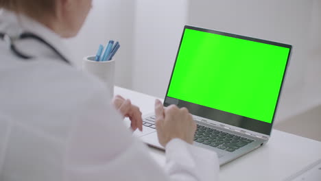 Eine-Ärztin-Schaut-Auf-Das-Grüne-Display-Eines-Laptops-Und-Sucht-Nach-Chroma-Key-Technologie,-Die-Online-Per-Video-Chat-Oder-Videoanruf-Kommuniziert