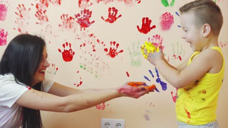 gelukkige moeder en haar schattige jongen hebben samen plezier en laten hun kleurrijke handsporen op de muur achter. jonge gelukkige familie. moeder en kind concept