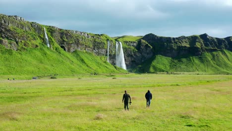 fotógrafos de naturaleza caminando sobre un campo de hierba verde hacia seljalandsfoss en islandia