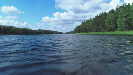 aerial shot above a dark blue river in sweden at daytime, surrounded with green forest and a blue sky with scattered clouds