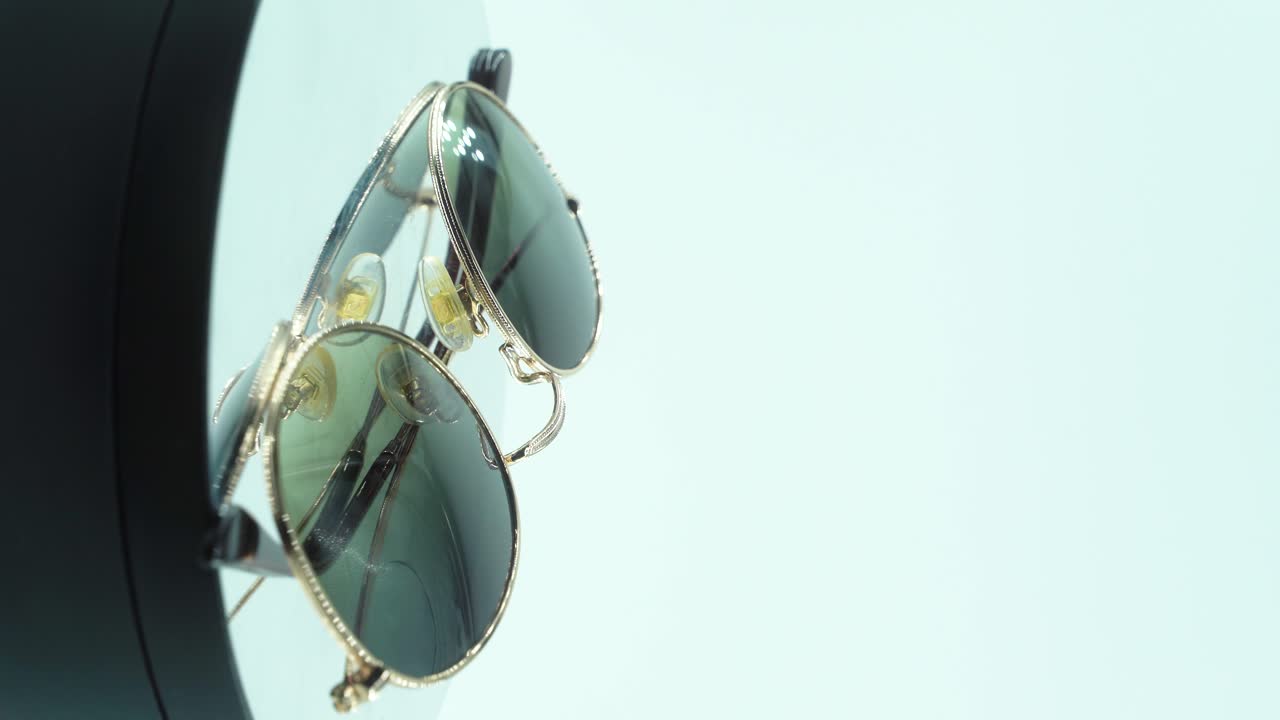 360 회전 반사 스탠드, 스튜디오 조명, 제품 4k 비디오, 느린 동작에 금색 선글라스를 놓는 수직 클로즈업 영화 촬영