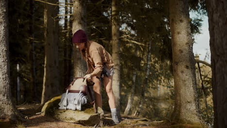 Young-woman-keeping-backpack-and-travel-mug-on-rock