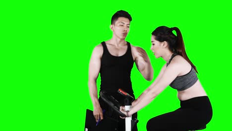 trainer helping woman to workout on bicycle