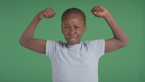 Studio-Shot-Of-Young-Boy-Showing-Off-Muscles-Against-Green-Background