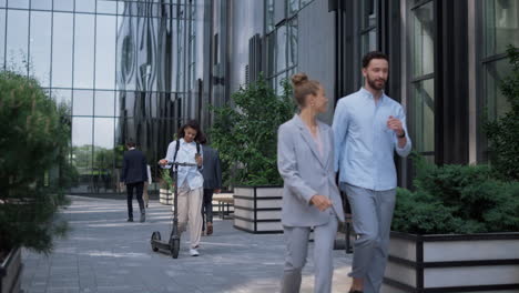 smiling manager walking holding electric scooter near modern office building.