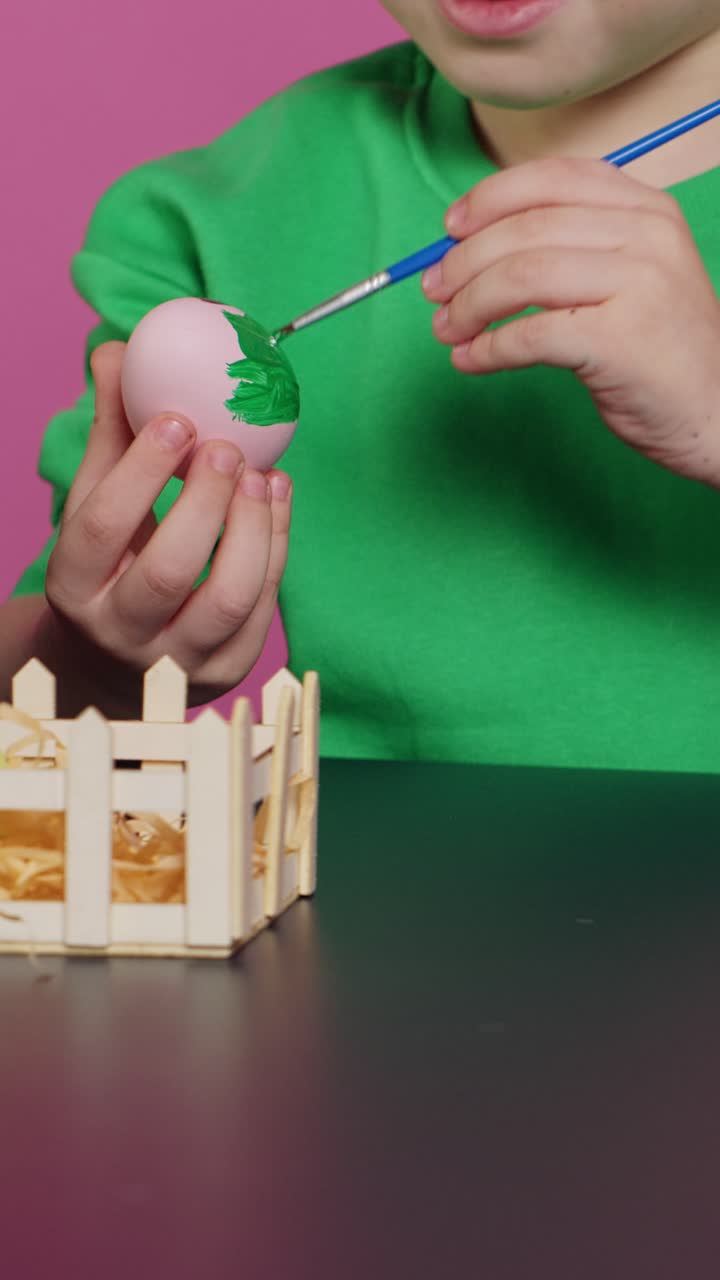 Child's Hands Painting a Pink Easter Egg with Green Paint