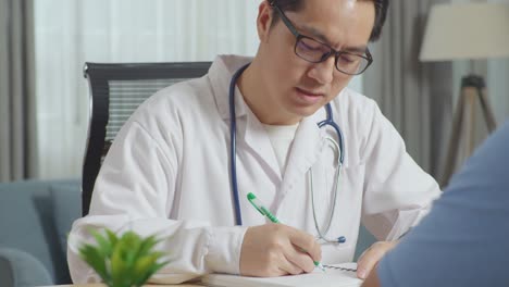 close up of asian male doctor talking to a male patient and writing prescription in clinic