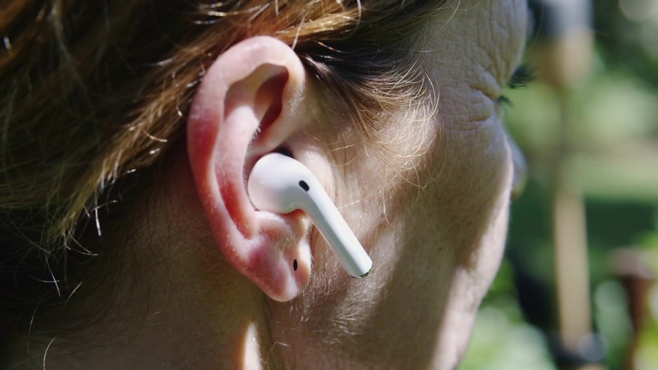 Inizio, telecamera che segue una donna che muove la testa in giardino, mostrando l'uso di auricolari bianchi, spazio per il testo