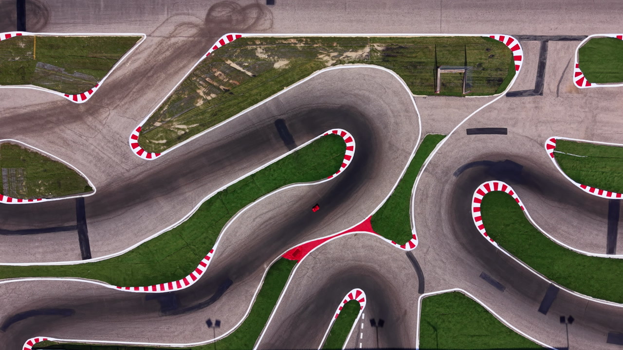 Top-down view of a winding RC car race track with red and white curbs, smooth asphalt curves, and green grass infields