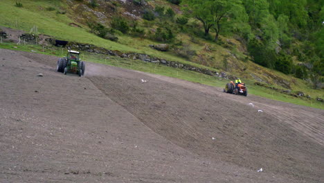 trackers plowing the fields on a steep mountain while birds are flying by