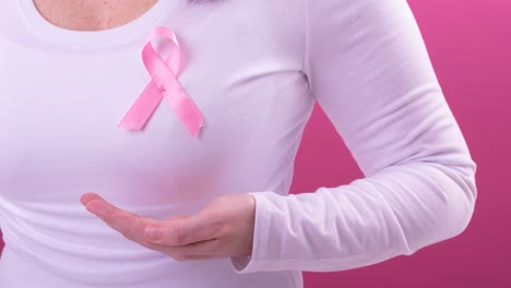 Video-of-midsection-of-caucasian-woman-wearing-pink-cancer-awareness-ribbon,-with-pink-background