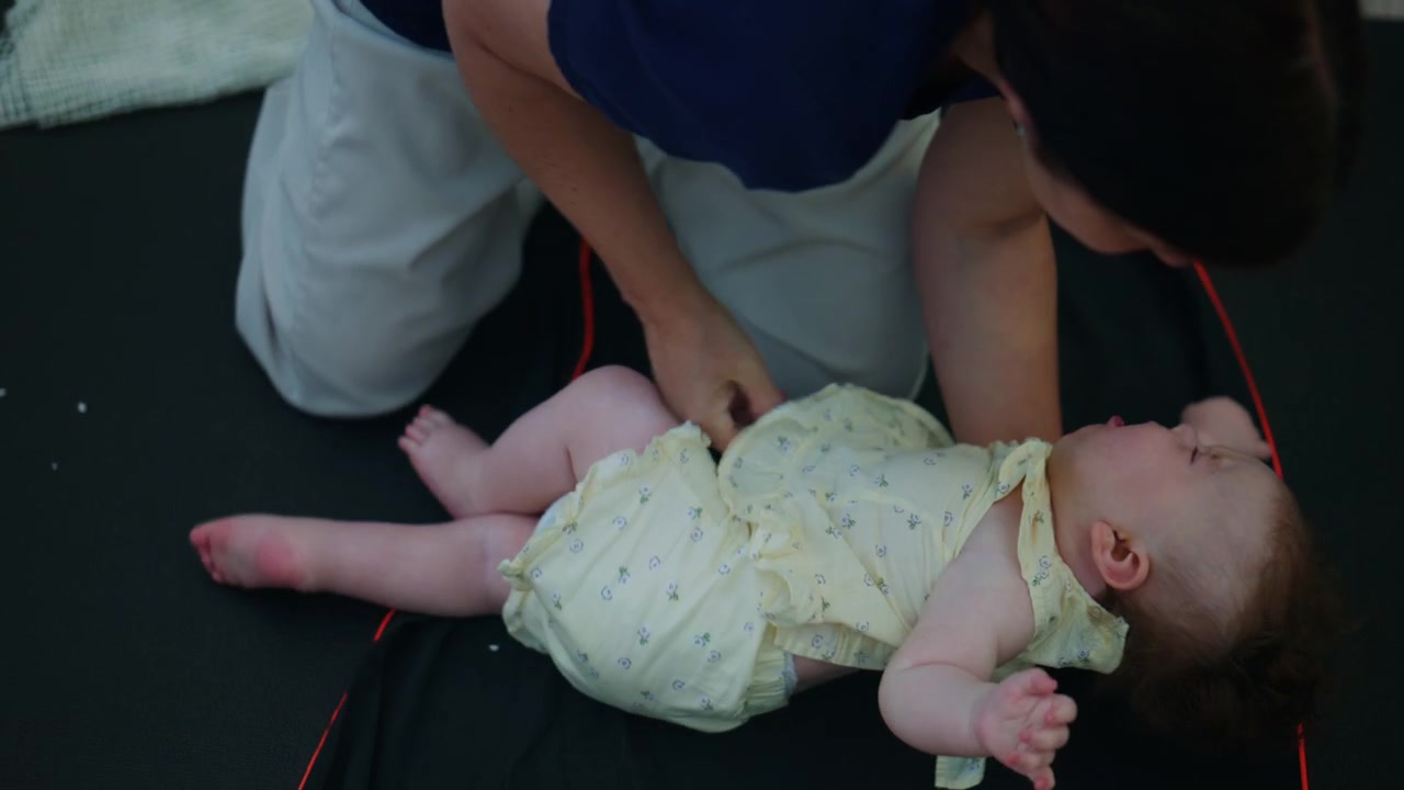 Bambino tenuto in posizione eretta da un adulto su un tappetino morbido, creando un momento di genitorialità naturale, cura e sviluppo del bambino.
