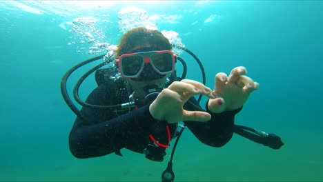 mujer disfrutando del buceo saludando a la cámara bajo el agua fhd
