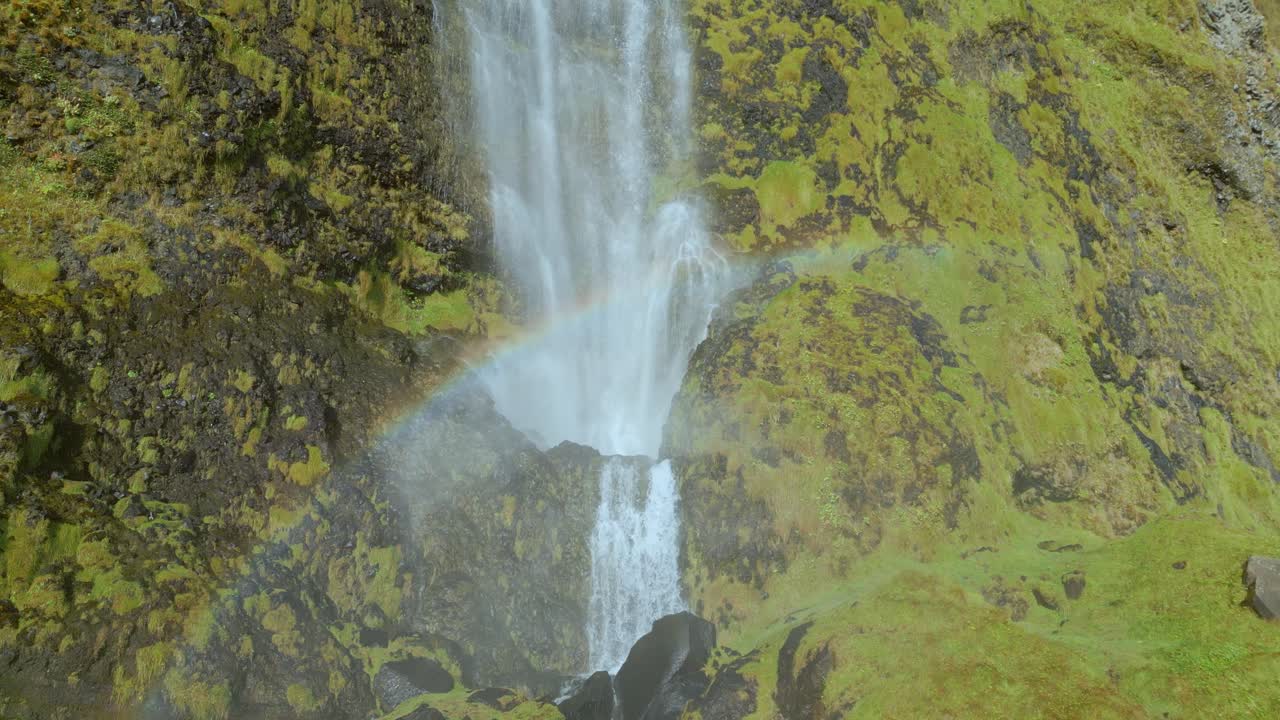 agua que cae en cascada por una cascada con un arco iris y musgo verde que cubre el acantilado rocoso