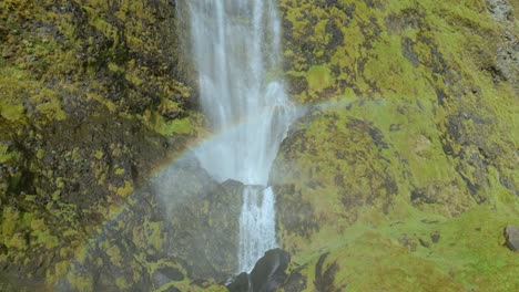 water-cascading-down-a-waterfall-with-a-rainbow-and-green-moss-covering-the-rocky-cliff-face