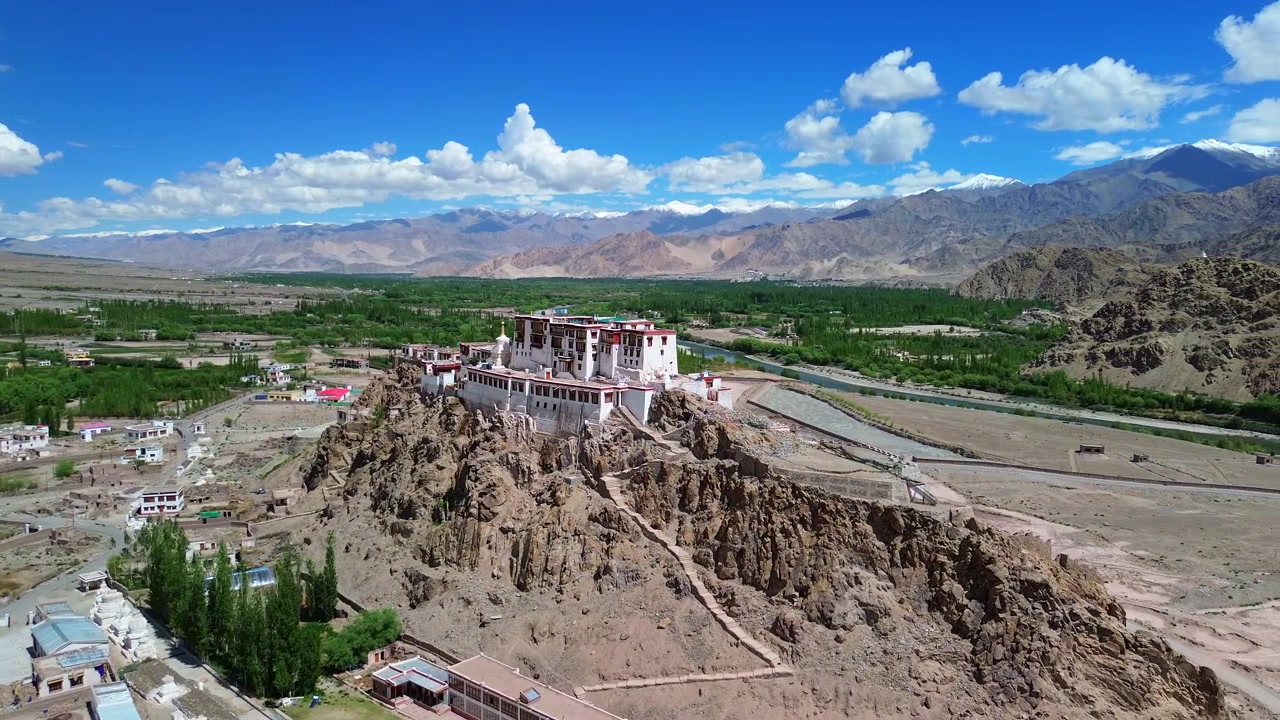 Cinematisk drönarfilmning med långsam bågrörelse som kretsar runt Stakna-klostrets vita tibetanska arkitektur på en kulle, avslöjande den slingrande Indusfloden, den gröna dalen och de karga bergen i Leh Ladakh, Indien