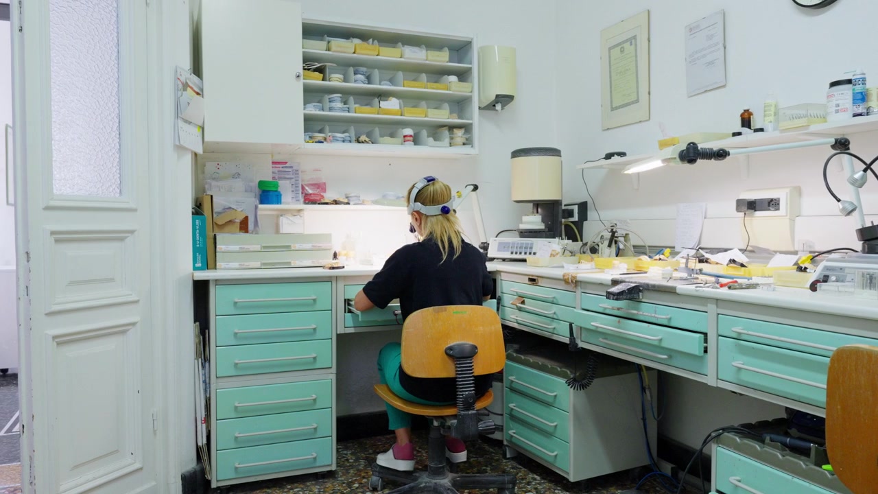 Kvindelig tekniker fremstiller tandproteser ved arbejdsbænk i et dentallaboratorium.