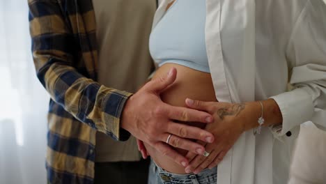 Close-up-of-a-happy-middle-aged-man-stroking-the-belly-of-his-pregnant-wife-while-standing-at-home