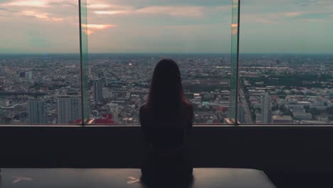 la chica se sienta y mira la vista de bangkok en la azotea de la torre baiyoke al atardecer