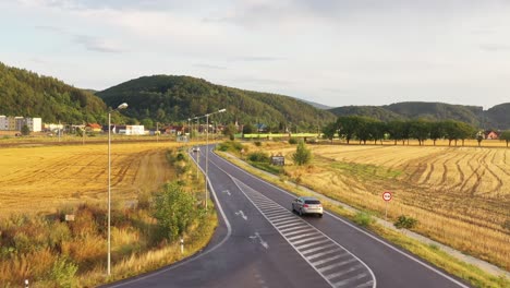 Long-aerial-drone-shot-of-silver-car-on-the-asphalt-road