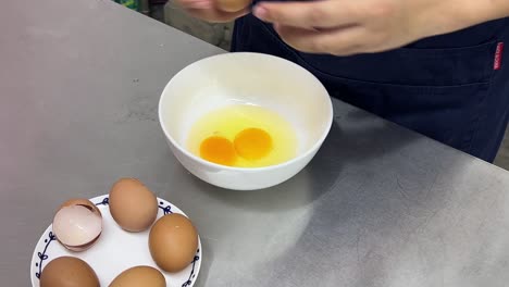 Close-up-shot-of-pastry-dessert-making-in-progress,-patissier-cracking-eggs-into-bowl-commercial-restaurant-setting