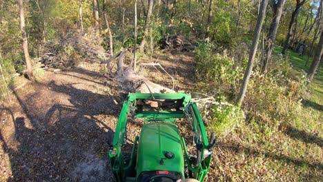 punto de vista de ángulo alto en un pequeño tractor verde usando horquillas elevadoras para mover un tocón de árbol