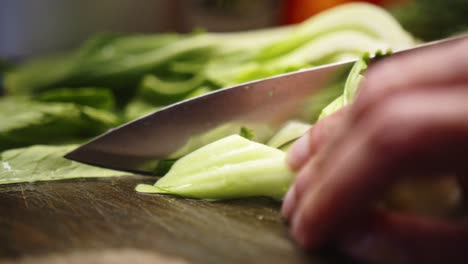asian chef slices leafy green vegetable with sharp knife.