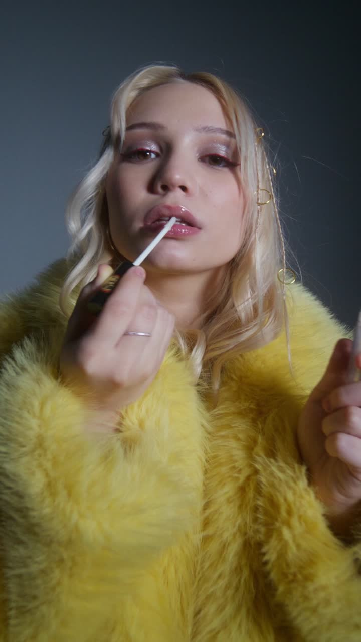 mujer aplicando lápiz labial en abrigo de piel amarillo