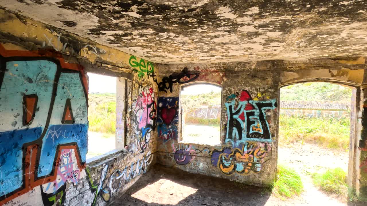 Camera pans inside sunlit abandoned fort, revealing colorful graffiti and bright outdoor scenery
