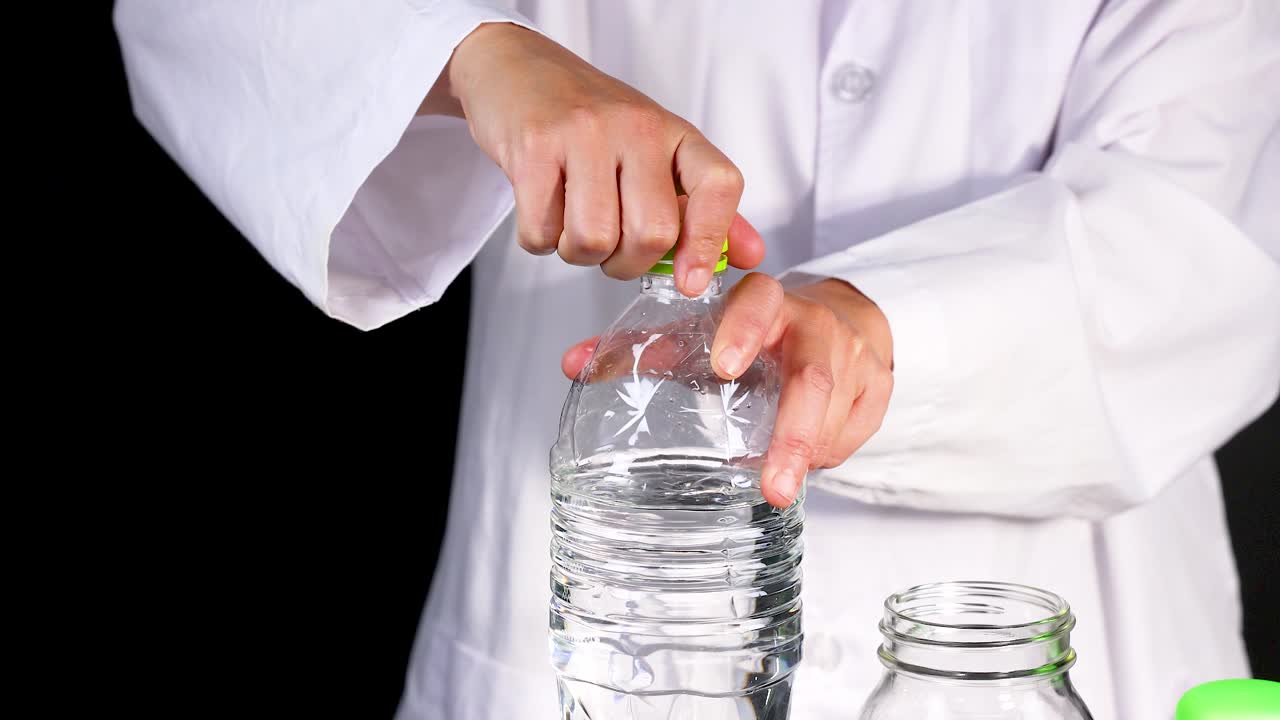 un científico con una bata de laboratorio abre una botella de agua, preparándose para un experimento químico con un vaso
