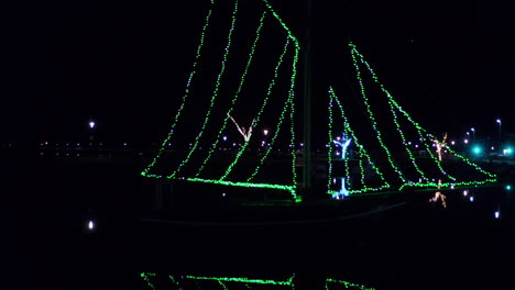drone tracking right with galway hooker boats strung up with green string lights sparkling in water at night