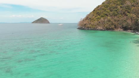 Emerald-shallow-shoreline-and-lush-green-coast-of-Banana-Beach-in-Coral-Island-,-Thailand---Aerial-Low-angle-Fly-over-shot