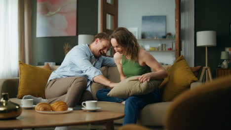 carefree lovers playing pillow fight at home couch. laughing couple having fun