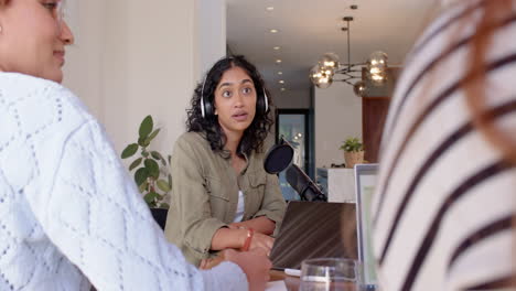 recording podcast, woman with headphones speaking into microphone with female friends