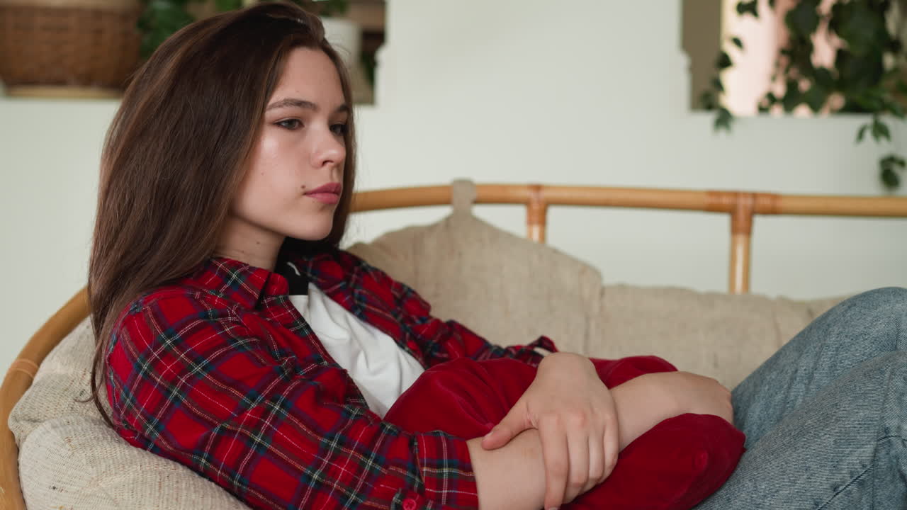 печальная женщина сидит в кресле и держит подушку. дама отправляется в тяжелое путешествие интроспекции, находя мимолетные моменты отдыха. эмоциональная суматоха