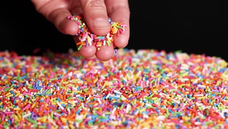 hand interacting with rainbow sprinkles on surface