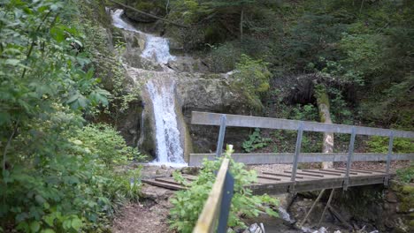 Toma-En-Cámara-Súper-Lenta-De-Cascada-Que-Fluye-Por-La-Montaña-Y-Puente-De-Madera