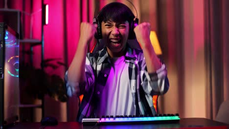 front view of excited asian teen boy gamer celebrates victory while playing video game on computer
