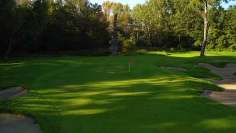 Umlaufbahn-Mit-Niedrigem-Winkel,-Die-Einen-Dron-Schuss-Etabliert,-Der-Tief-In-Bodennähe-über-Dem-Golfplatz-Fliegt-Und-Bunker,-Flagge,-Grün-Um-Bäume-Während-Eines-Sonnigen-Tages-In-Warschau,-Polen,-Zeigt