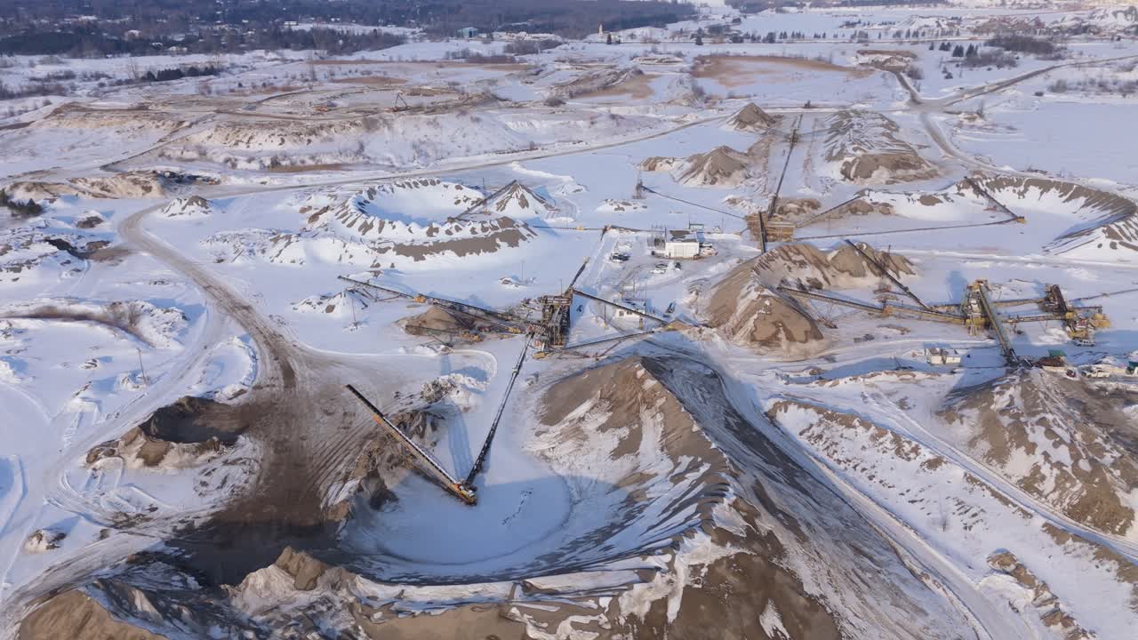 Winter drone footage of a gravel pit in Caledon, Ontario, Canada. Snow covered terrain, extraction areas, access roads, and industrial landforms appear beneath a sunny winter sky