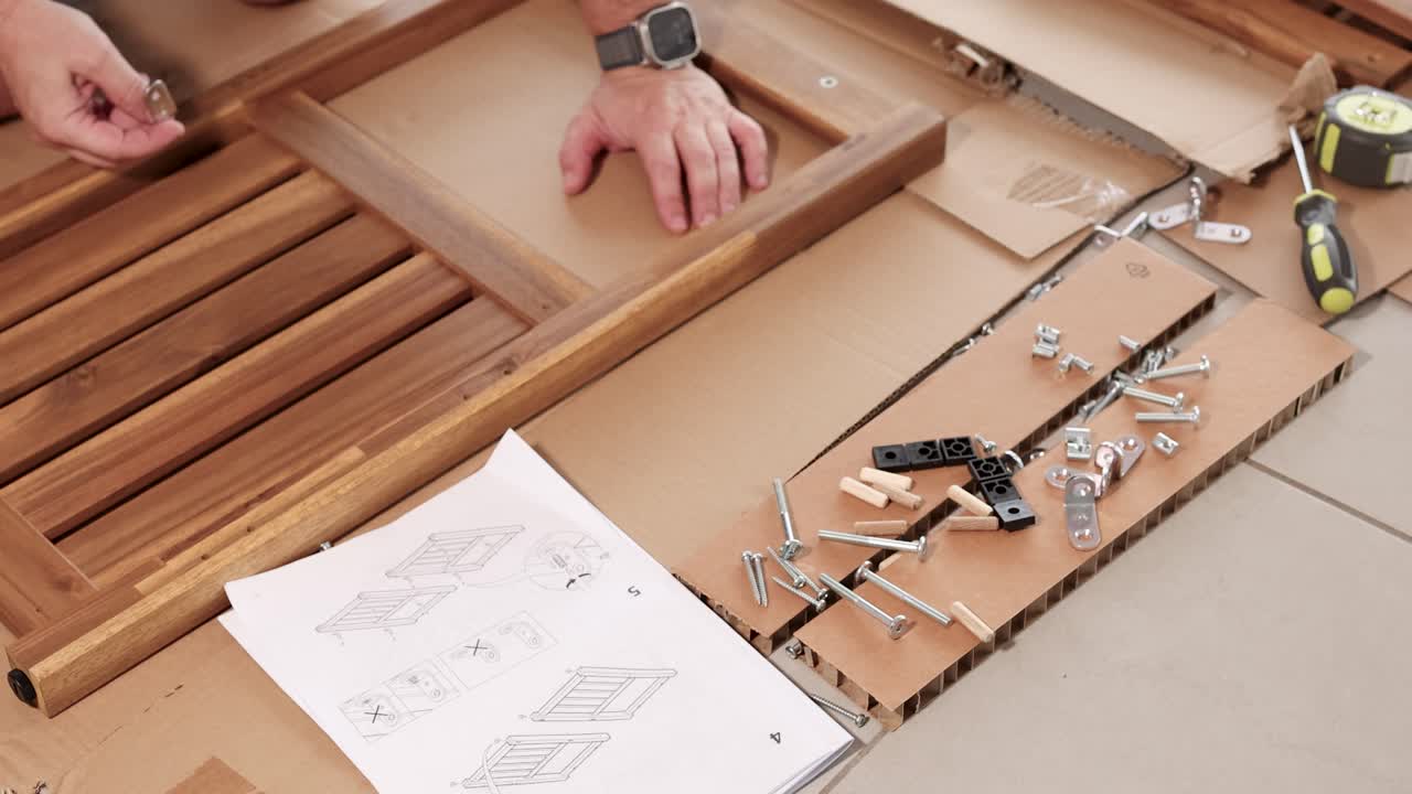 Hands assembling wooden furniture using tools and instructions. Bright lighting highlights detailed steps on a tiled floor