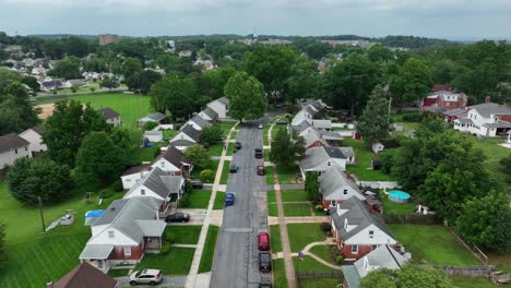 quiet american suburb with identical single-family homes, tree-lined streets, green lawns and peaceful small-town atmosphere. aerial flyover shot. cloudy day in summer