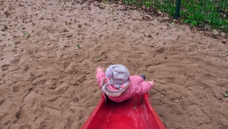 young caucasian toddler girl playing on public playground slide on cold autumn day