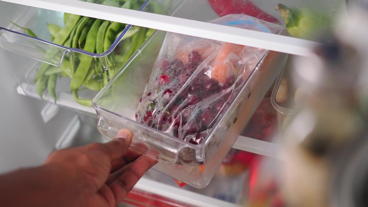 Persona che chiude il cassetto del frigorifero con frutti di bosco surgelati