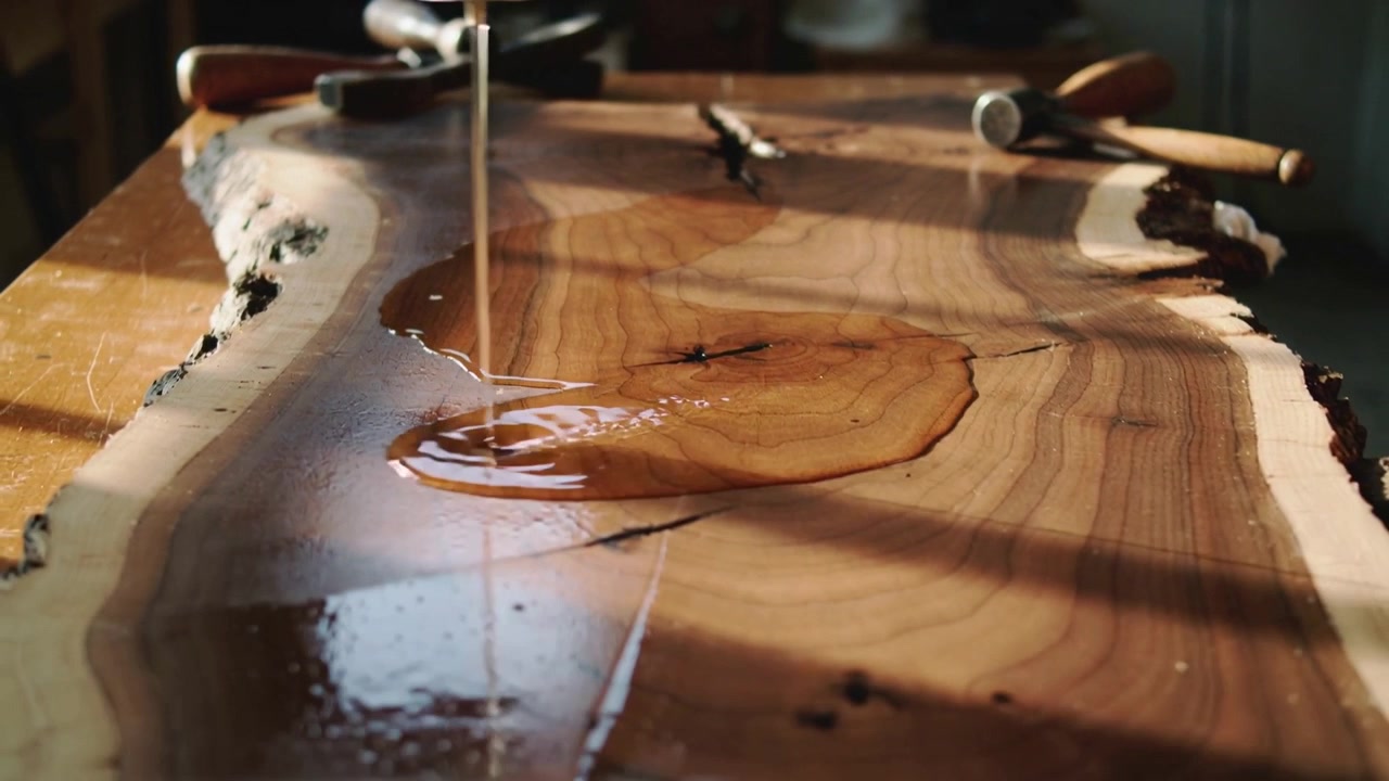 Ugello stretto che cola resina ambrata su una tavola di legno a bordo vivo su un banco, evidenziando le venature.