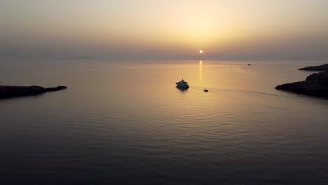 Una-Fascinante-Toma-Aérea-Del-Mar-En-Loutra,-Kythnos-Durante-El-Amanecer,-Siguiendo-Un-Yate