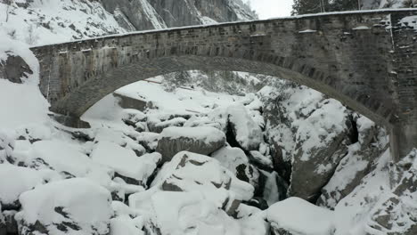 Drone-flying-underneath-stone-bridge-over-a-small-stream